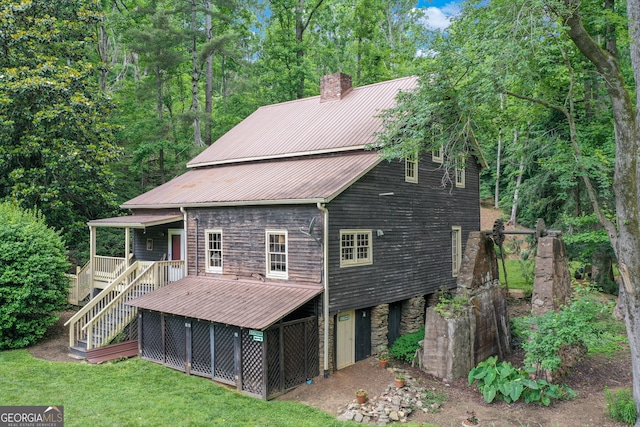 back of property featuring a lawn, stone siding, a chimney, stairway, and metal roof