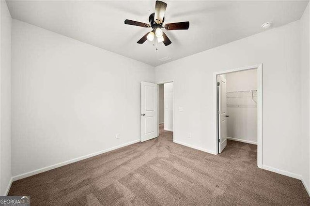 unfurnished bedroom featuring a spacious closet, a closet, ceiling fan, and carpet