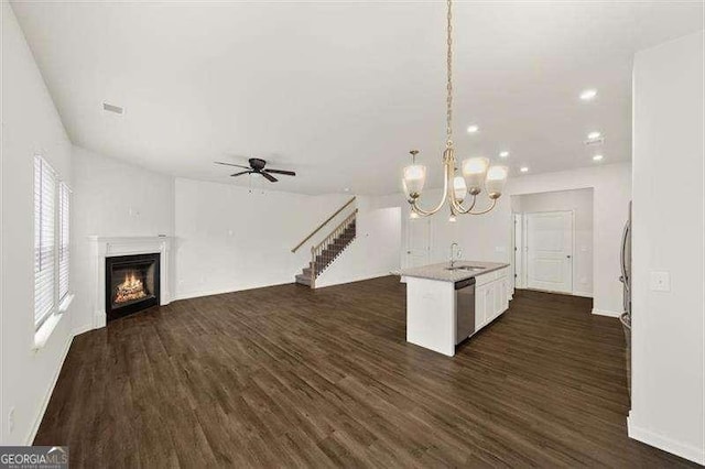 kitchen featuring dark wood-type flooring, hanging light fixtures, a center island with sink, stainless steel dishwasher, and white cabinets