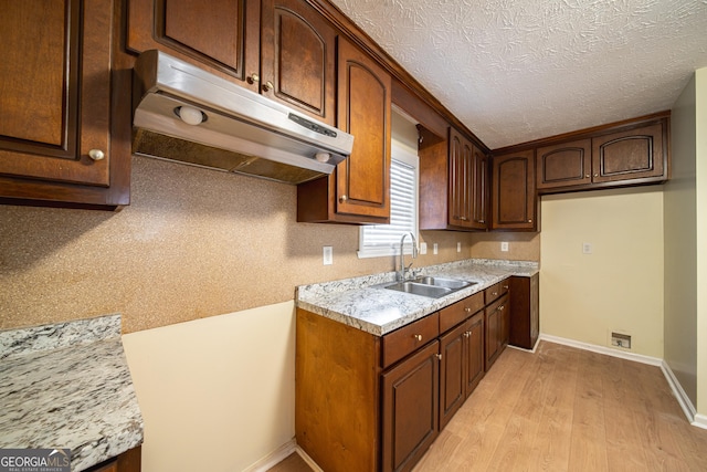 kitchen with light stone counters, sink, light hardwood / wood-style flooring, and a textured ceiling