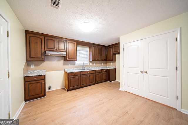 kitchen with sink, light wood-type flooring, dark brown cabinetry, light stone counters, and a textured ceiling