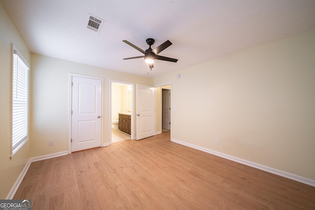 unfurnished bedroom featuring multiple windows, ceiling fan, light wood-type flooring, and ensuite bath