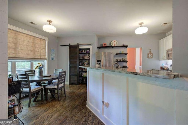 kitchen with white cabinetry, stainless steel appliances, dark hardwood / wood-style floors, light stone counters, and a barn door