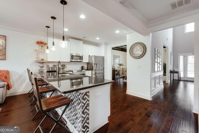 kitchen featuring pendant lighting, appliances with stainless steel finishes, white cabinetry, a kitchen bar, and kitchen peninsula