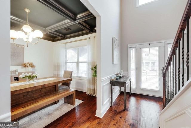 foyer entrance with dark wood-type flooring, coffered ceiling, an inviting chandelier, and beamed ceiling