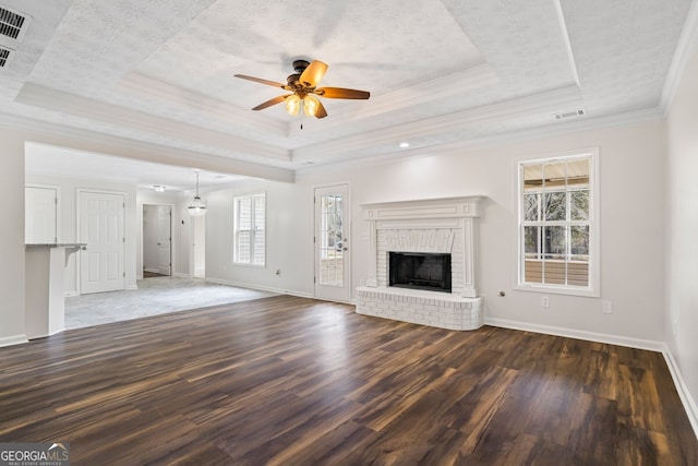 unfurnished living room featuring dark wood-type flooring, a raised ceiling, a brick fireplace, and a wealth of natural light