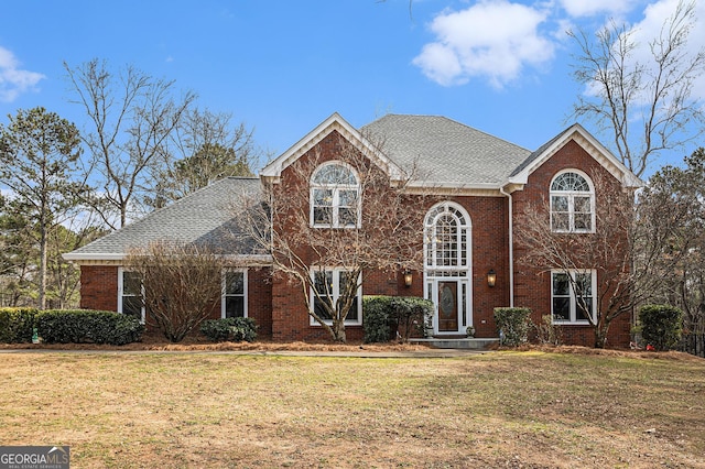 view of front of home featuring brick siding, a front lawn, and roof with shingles