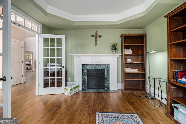 unfurnished living room featuring french doors, a raised ceiling, ornamental molding, a high end fireplace, and wood finished floors