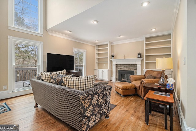 living room featuring light wood-style flooring, crown molding, a wealth of natural light, and a stone fireplace