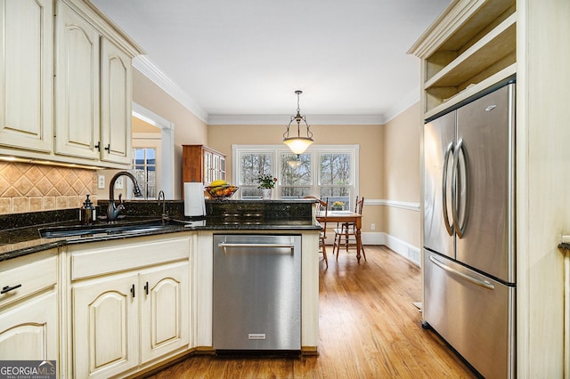 kitchen with light wood-style flooring, stainless steel appliances, a peninsula, a sink, and cream cabinetry