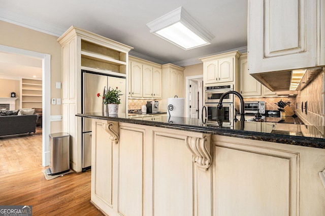 kitchen with cream cabinets, light wood-style flooring, a fireplace, ornamental molding, and appliances with stainless steel finishes