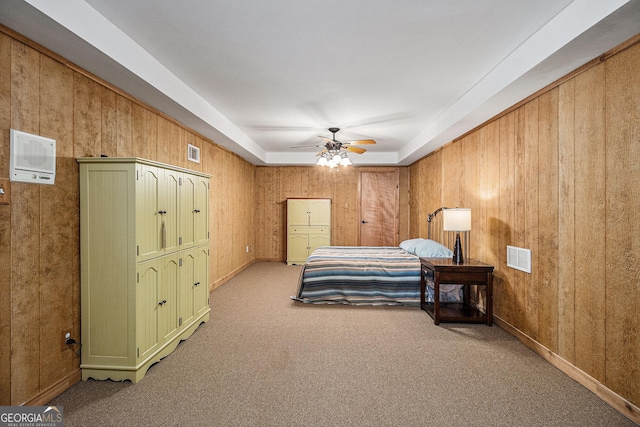 carpeted bedroom featuring ceiling fan, wood walls, a raised ceiling, and visible vents