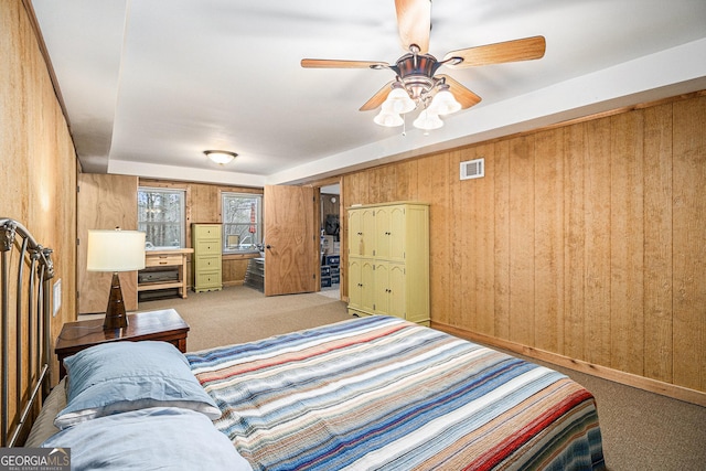 bedroom with a ceiling fan, carpet flooring, visible vents, and wooden walls