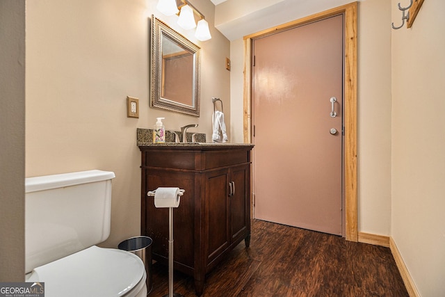 half bath featuring baseboards, vanity, toilet, and wood finished floors