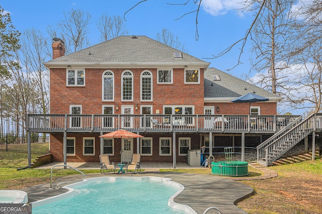 rear view of house with a deck, a patio, brick siding, and a chimney