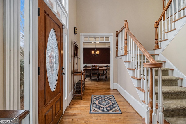 entryway featuring a chandelier, a wealth of natural light, light wood-type flooring, and a towering ceiling