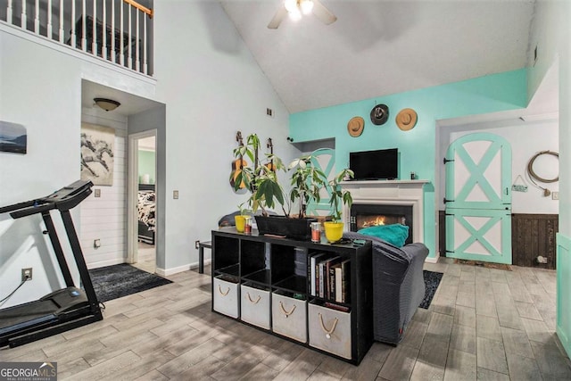 living room featuring a warm lit fireplace, baseboards, a ceiling fan, wood tiled floor, and high vaulted ceiling