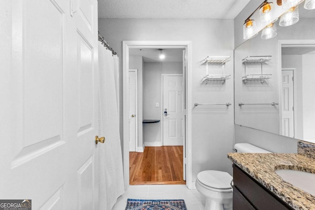 bathroom with tile patterned flooring, vanity, a textured ceiling, and toilet