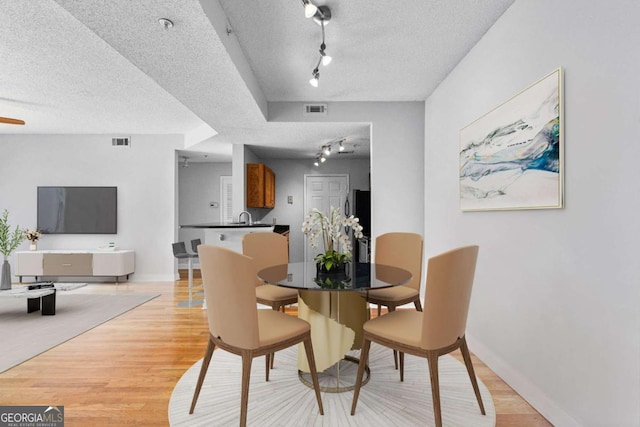 dining area with rail lighting, sink, a textured ceiling, and light hardwood / wood-style flooring