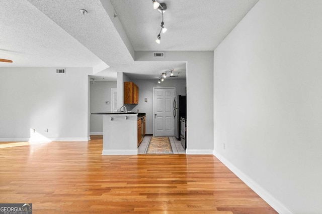 kitchen with sink, a textured ceiling, light hardwood / wood-style floors, and kitchen peninsula