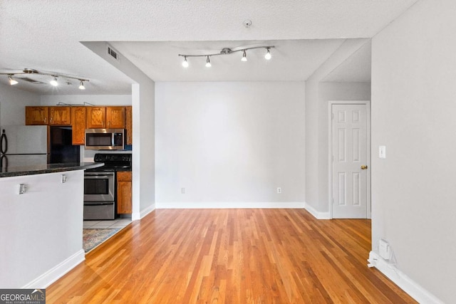 kitchen with stainless steel appliances, a textured ceiling, and light hardwood / wood-style floors