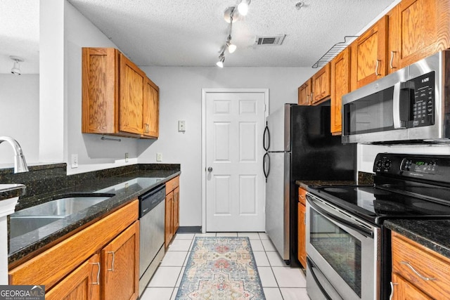 kitchen with light tile patterned floors, appliances with stainless steel finishes, sink, and dark stone countertops