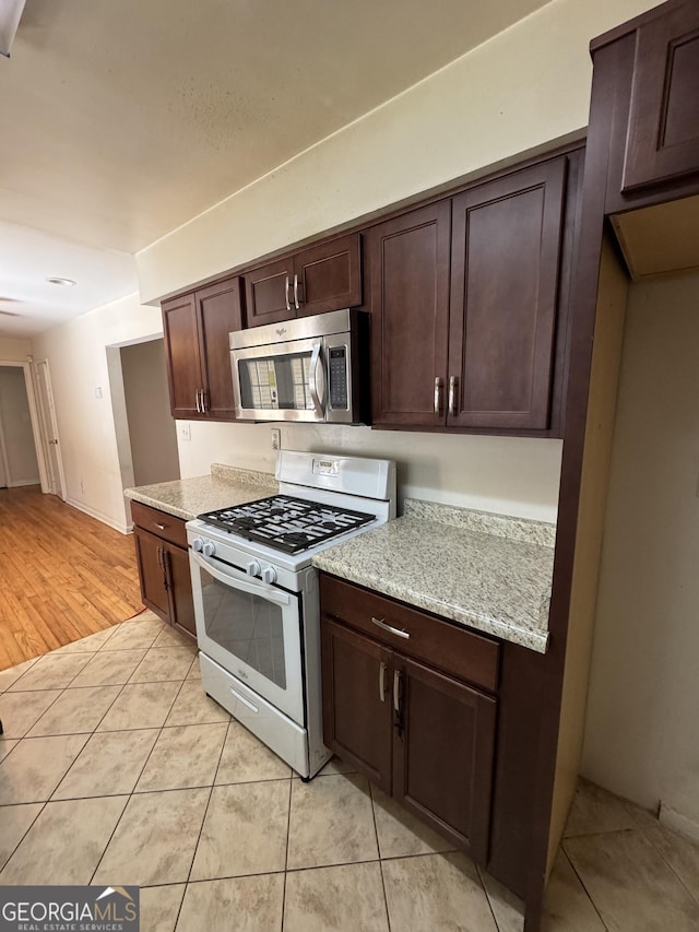 kitchen featuring light stone countertops, white gas stove, dark brown cabinets, and light tile patterned floors