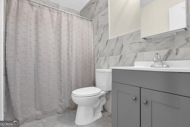 bathroom with toilet, a shower with curtain, tile patterned floors, vanity, and tile walls