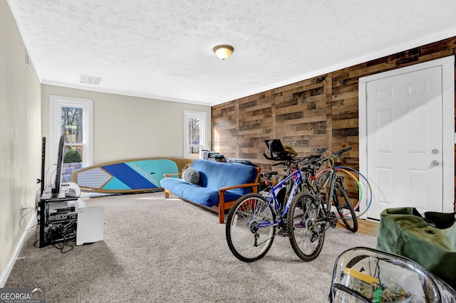 living area featuring a textured ceiling, wood walls, carpet flooring, and visible vents