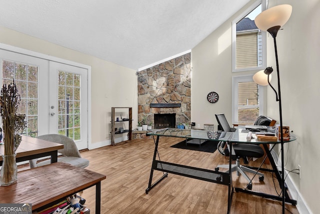 office with a textured ceiling, lofted ceiling, a fireplace, french doors, and light wood finished floors