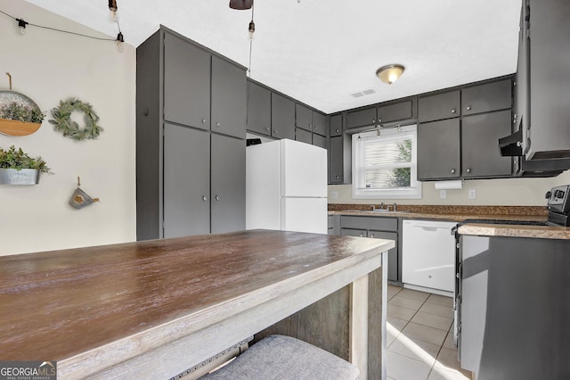 kitchen with white appliances, light tile patterned floors, visible vents, dark countertops, and a sink