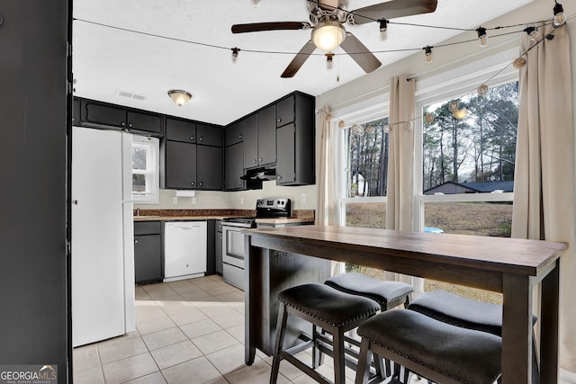 kitchen featuring white appliances, visible vents, ceiling fan, dark cabinets, and light tile patterned flooring