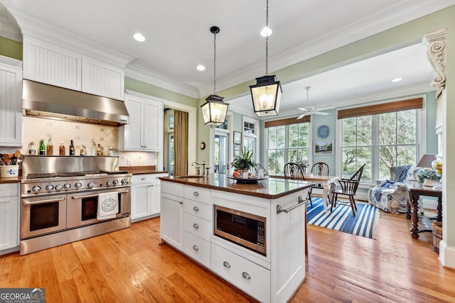 kitchen featuring decorative light fixtures, ventilation hood, appliances with stainless steel finishes, a kitchen island with sink, and white cabinets