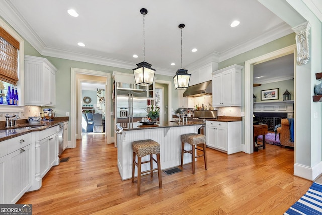 kitchen with sink, white cabinetry, a kitchen island, pendant lighting, and range hood