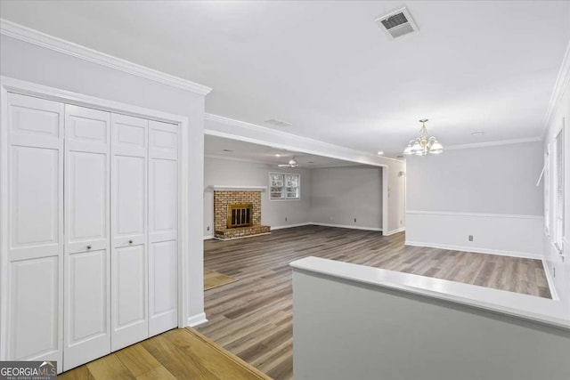 unfurnished living room featuring crown molding, wood-type flooring, a fireplace, and a chandelier