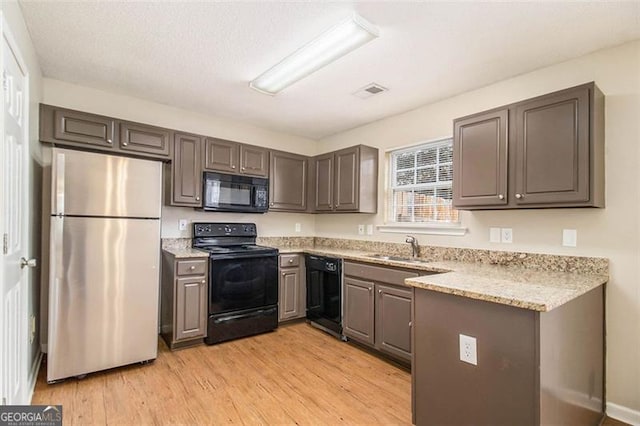 kitchen with light stone countertops, sink, light hardwood / wood-style floors, and black appliances