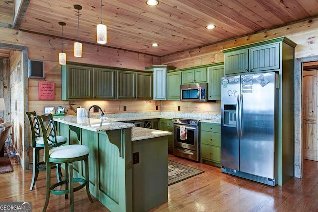 kitchen featuring light stone counters, green cabinetry, stainless steel appliances, and pendant lighting