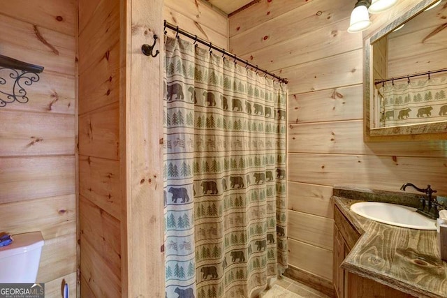 bathroom featuring vanity, wooden walls, toilet, and walk in shower