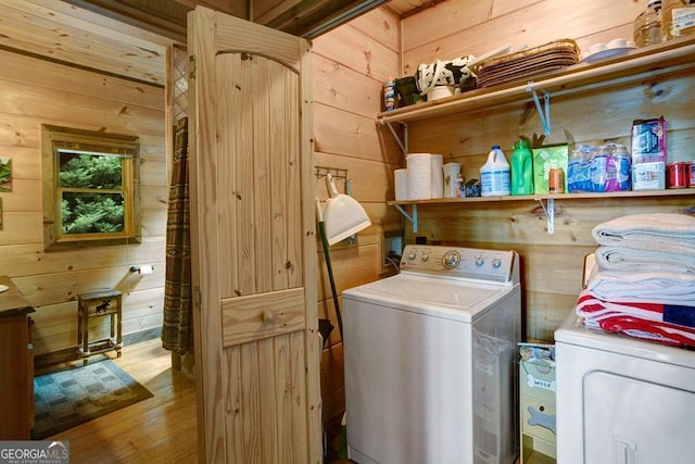 laundry room featuring washing machine and clothes dryer, wooden walls, and light hardwood / wood-style floors