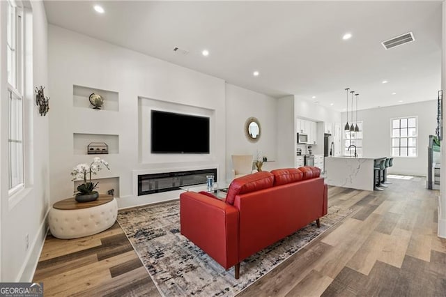 living area featuring recessed lighting, visible vents, a glass covered fireplace, and light wood-style flooring
