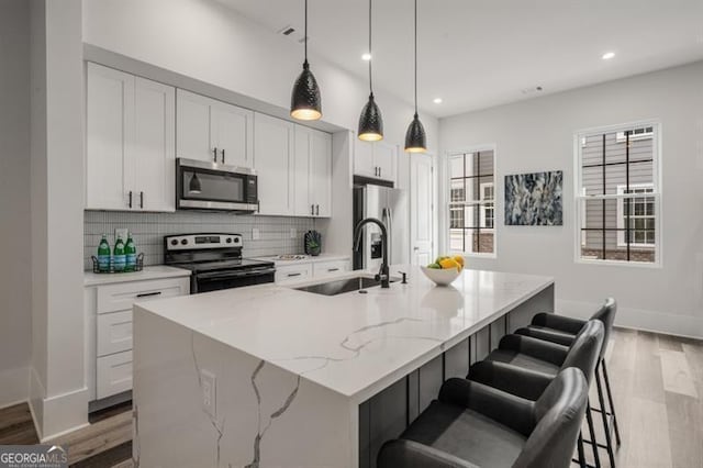 kitchen featuring an island with sink, a sink, appliances with stainless steel finishes, white cabinetry, and tasteful backsplash