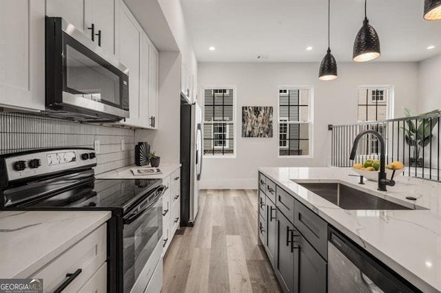 kitchen featuring pendant lighting, a sink, backsplash, light wood-style floors, and appliances with stainless steel finishes