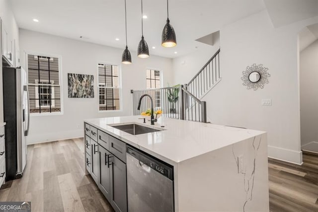 kitchen with baseboards, a center island with sink, light wood-style flooring, a sink, and appliances with stainless steel finishes
