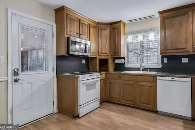 kitchen featuring light wood-style flooring, white appliances, a sink, brown cabinetry, and dark countertops