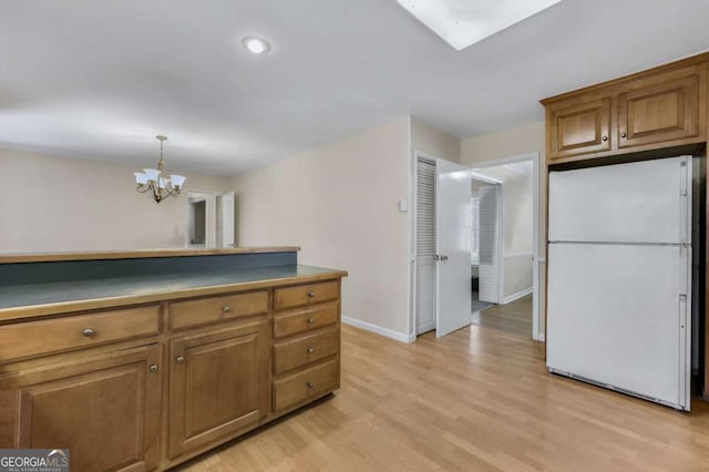 kitchen with brown cabinets, freestanding refrigerator, a chandelier, light wood-type flooring, and baseboards