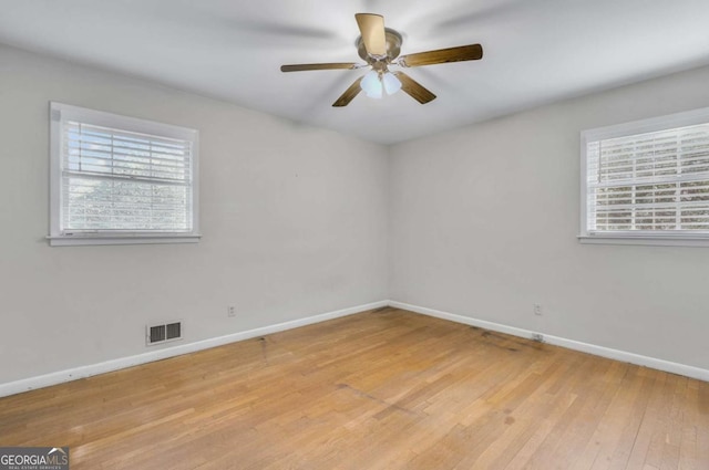 empty room featuring light wood finished floors, baseboards, visible vents, and a wealth of natural light