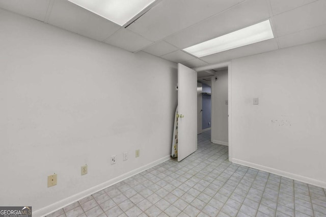 interior space featuring light floors, a drop ceiling, and baseboards