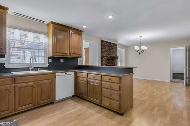 kitchen with brown cabinets, light wood-style flooring, white dishwasher, a sink, and a peninsula