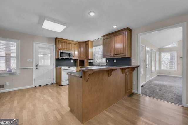 kitchen featuring brown cabinets, a breakfast bar area, white electric range, stainless steel microwave, and a peninsula