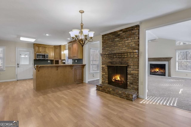 kitchen with brown cabinets, a fireplace, stainless steel microwave, open floor plan, and a kitchen breakfast bar